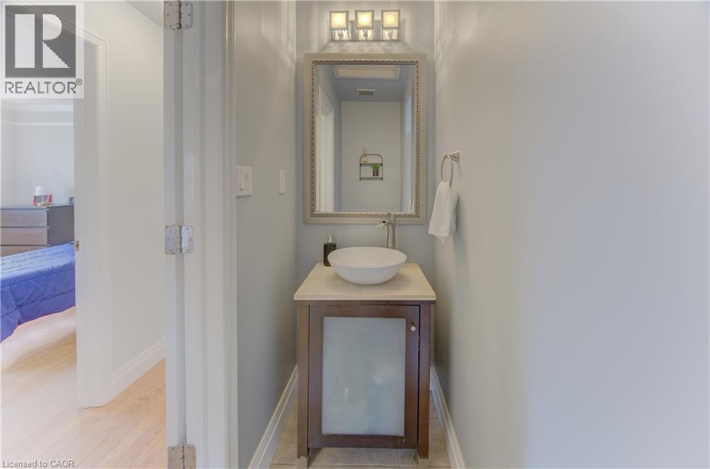 Powder room featuring a single-sink vanity with a vessel sink, light-toned countertop, and a decorative framed mirror with overhead lighting - 106 Autumn Hill Crescent, Kitchener, ON - Indoor