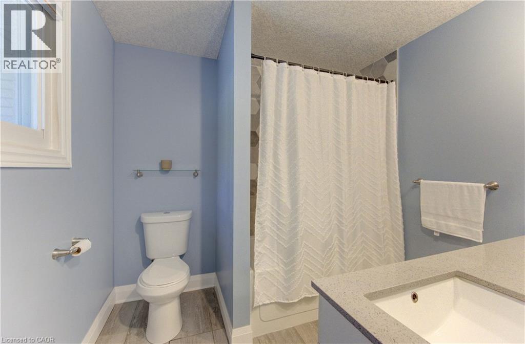 Contemporary bathroom featuring a window, wood-finish flooring, a white toilet, and a vanity with an integrated sink and light-toned countertop - 106 Autumn Hill Crescent, Kitchener, ON - Indoor Photo Showing Bathroom