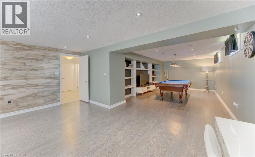 Finished recreation room featuring a modern wood-finish flooring, recessed lighting, and a prominent built-in media center with open shelving - 106 Autumn Hill Crescent, Kitchener, ON - Indoor Photo Showing Other Room