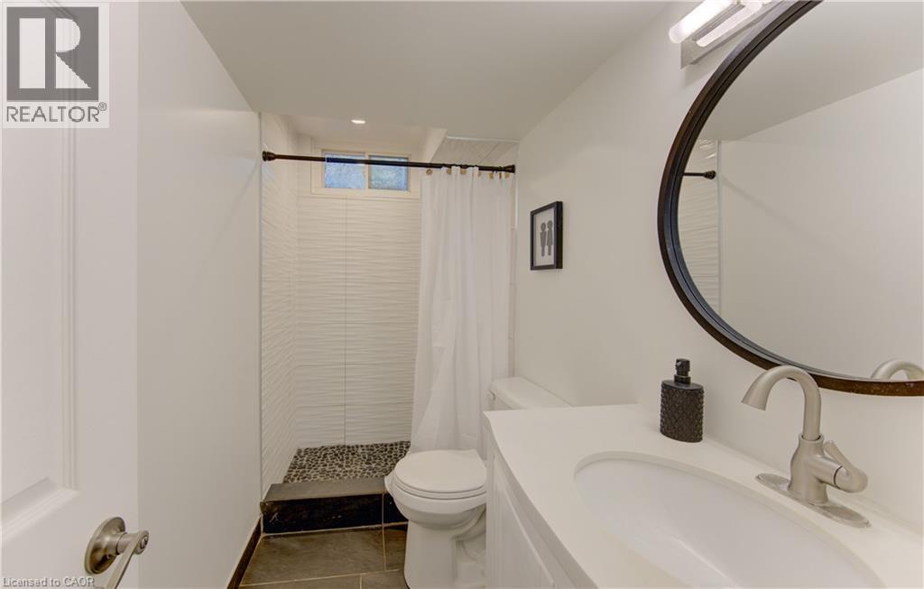 Bathroom featuring a walk-in shower with pebble tile flooring and white textured wall tile, a white vanity with an integrated sink, a brushed nickel faucet, and a round framed mirror - 106 Autumn Hill Crescent, Kitchener, ON - Indoor Photo Showing Bathroom