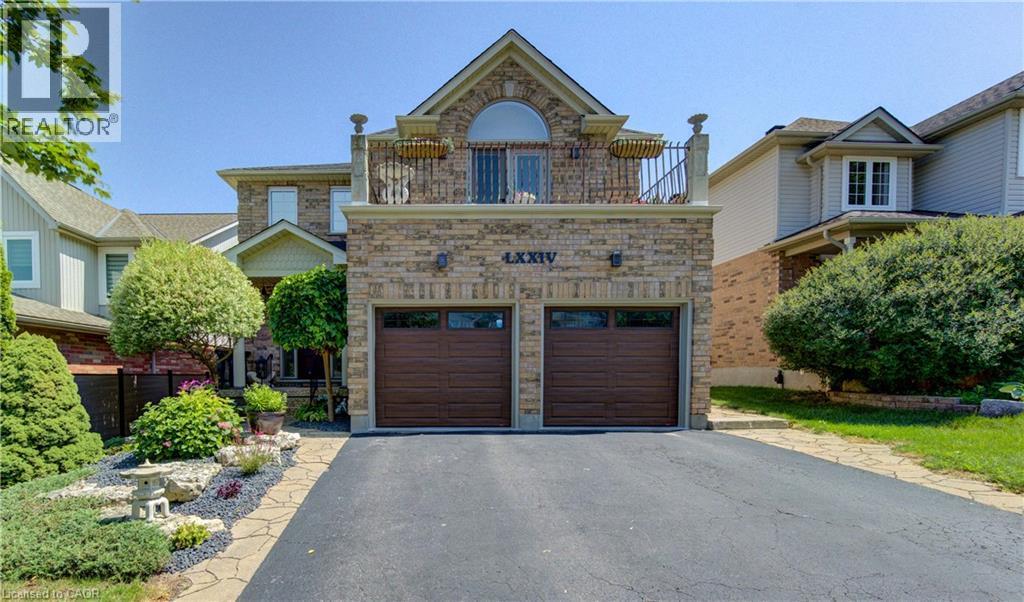 Stone facade home featuring a two-car garage with wood-finish doors, an upper-level balcony with a wrought iron railing, and an arched window - 74 Forest Edge Trail, Kitchener, ON