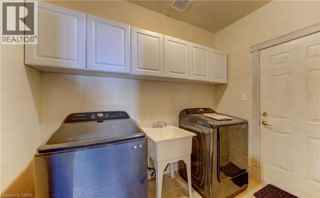 Laundry area featuring a utility sink, light-toned wall cabinets, and tile flooring - 74 Forest Edge Trail, Kitchener, ON