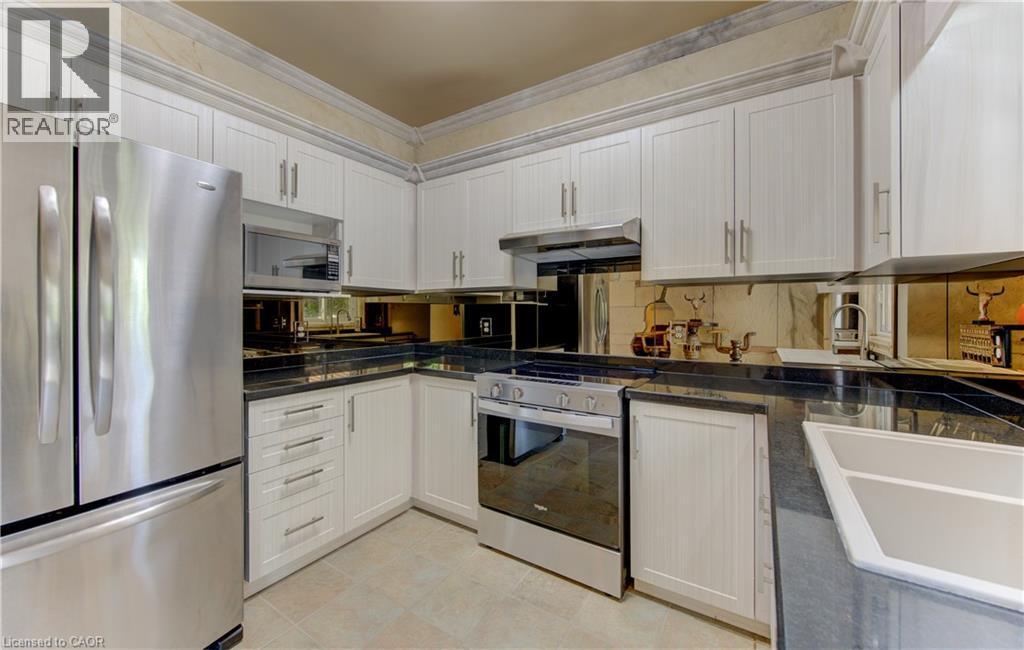 Kitchen featuring white cabinetry, dark countertops, stainless steel appliances, a mirrored backsplash, and tile flooring - 74 Forest Edge Trail, Kitchener, ON