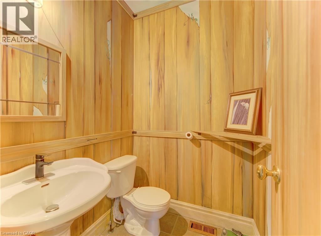 Powder room featuring wood-finish wall paneling, a white pedestal sink with a modern faucet, and a toilet - 74 Forest Edge Trail, Kitchener, ON