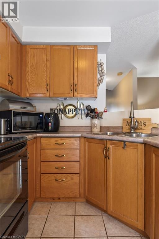 Kitchen featuring wood cabinetry, integrated sink, tile flooring, and a built-in oven - 10 Cadham Boulevard Unit# 29, Hamilton, ON - Indoor Photo Showing Kitchen With Double Sink