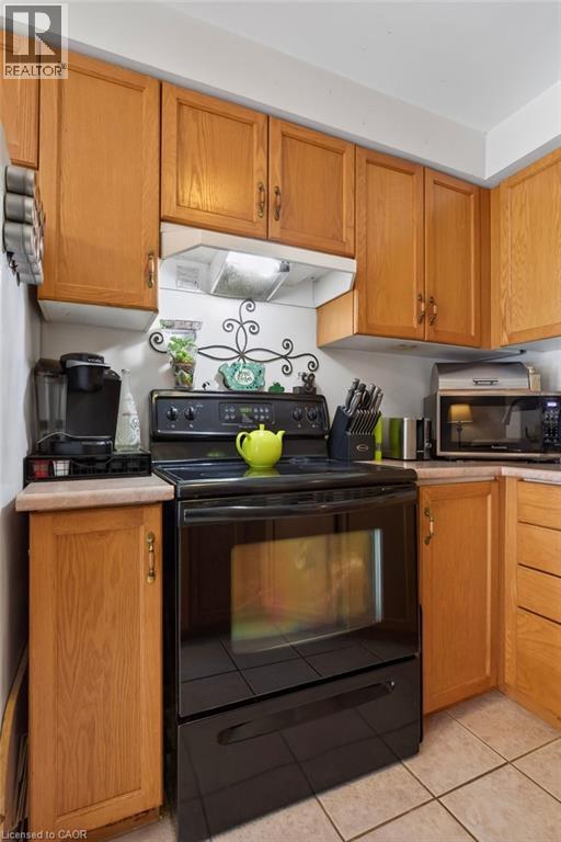 Wood-finish cabinetry, light-toned countertops, black built-in range, and tile flooring - 10 Cadham Boulevard Unit# 29, Hamilton, ON - Indoor Photo Showing Kitchen