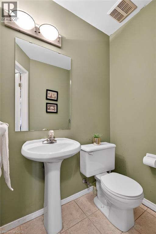 Pedestal sink with chrome faucet, wall-mounted mirror, overhead vanity lighting, and ceramic tile flooring - 10 Cadham Boulevard Unit# 29, Hamilton, ON - Indoor Photo Showing Bathroom