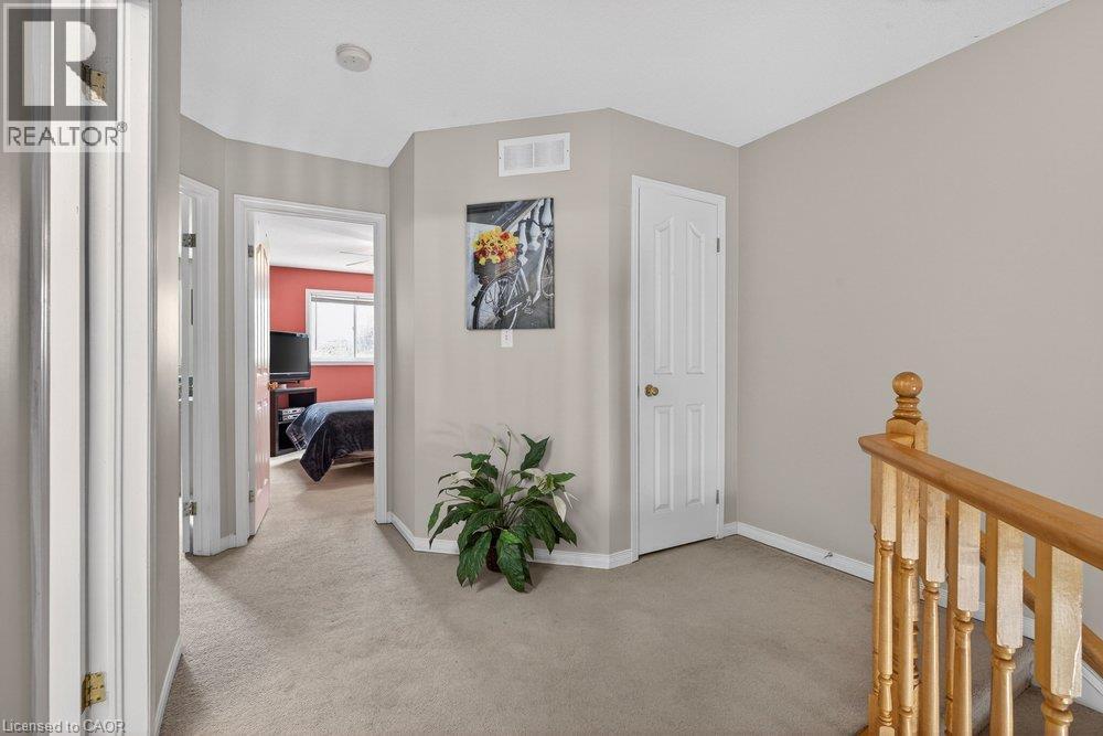 Carpeted hallway with light neutral wall paint, white trim, and a natural wood-finish staircase railing - 10 Cadham Boulevard Unit# 29, Hamilton, ON - Indoor Photo Showing Other Room