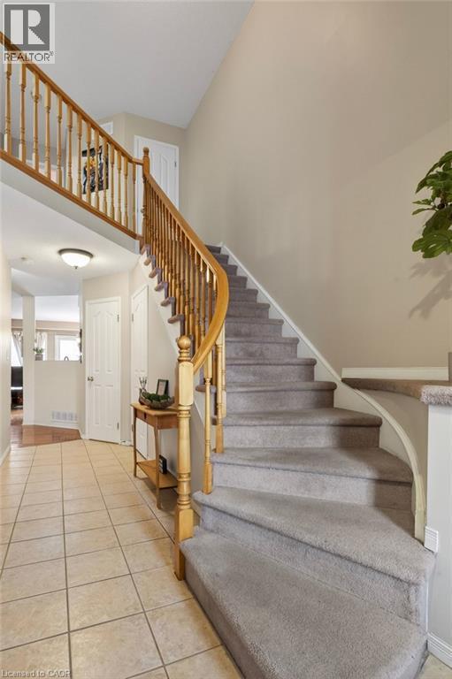 Tiled entry flooring with a carpeted curved staircase featuring wood banisters - 10 Cadham Boulevard Unit# 29, Hamilton, ON - Indoor Photo Showing Other Room