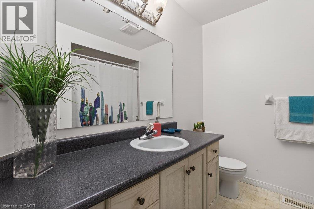Vanity with an integrated sink, dark countertop, light wood-finish cabinetry, and a wall-mounted mirror - 10 Cadham Boulevard Unit# 29, Hamilton, ON - Indoor Photo Showing Bathroom