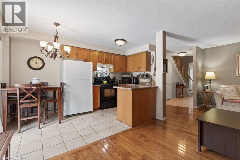 Hardwood flooring, tile flooring, wood-finish cabinetry, built-in kitchen appliances, and a staircase with wood handrails - 10 Cadham Boulevard Unit# 29, Hamilton, ON - Indoor Photo Showing Kitchen