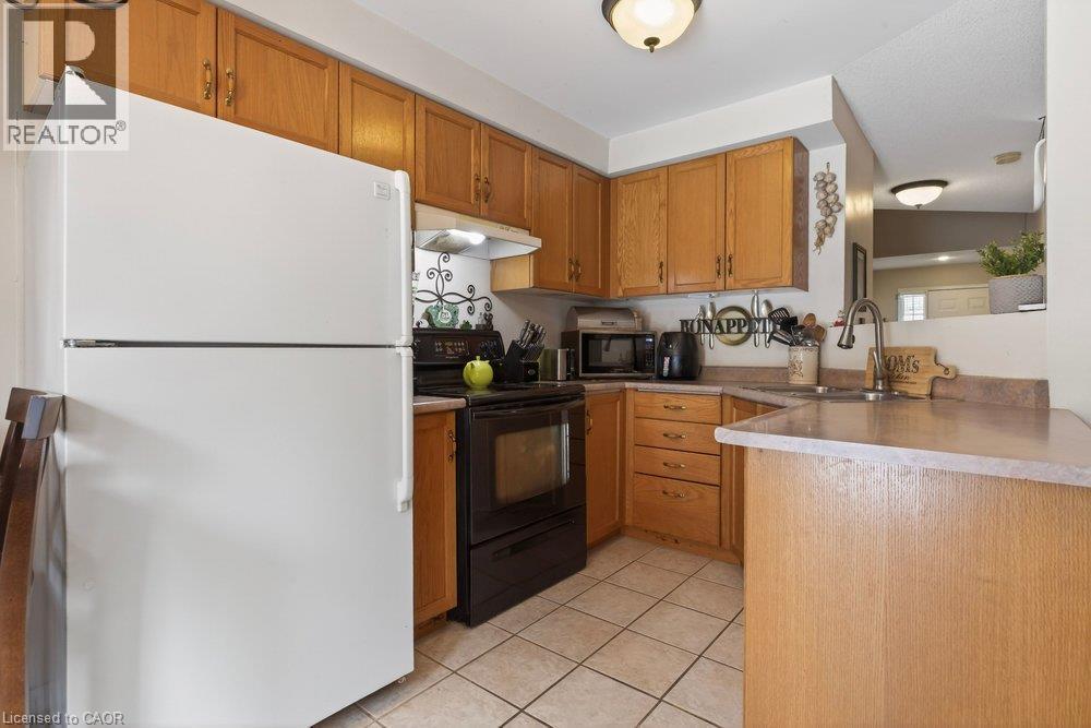 Efficient kitchen featuring wood-finish cabinetry, a built-in range, and tile flooring - 10 Cadham Boulevard Unit# 29, Hamilton, ON - Indoor Photo Showing Kitchen