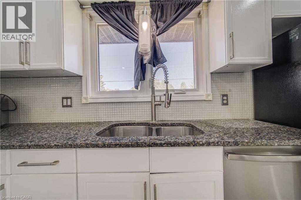 White cabinetry with brushed nickel hardware, granite countertops, tile backsplash, stainless steel sink with a gooseneck faucet, and a pendant light fixture - 161 Kipling Avenue, Kitchener, ON - Indoor Photo Showing Kitchen With Double Sink