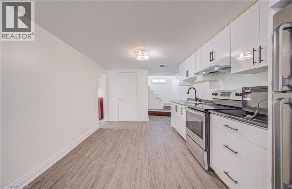 Kitchen featuring stainless steel appliances, black countertops, white cabinetry with black hardware, and wood-finish flooring - 161 Kipling Avenue, Kitchener, ON - Indoor Photo Showing Kitchen
