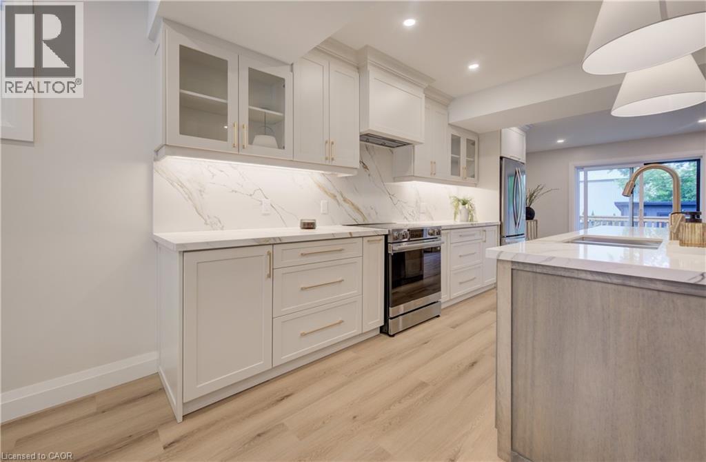 White cabinetry with glass-front accents, marble-look countertops and backsplash, stainless steel range, light wood-finish flooring, and a kitchen island with an integrated sink - 34 Moore Avenue N, Waterloo, ON - Indoor Photo Showing Kitchen With Upgraded Kitchen