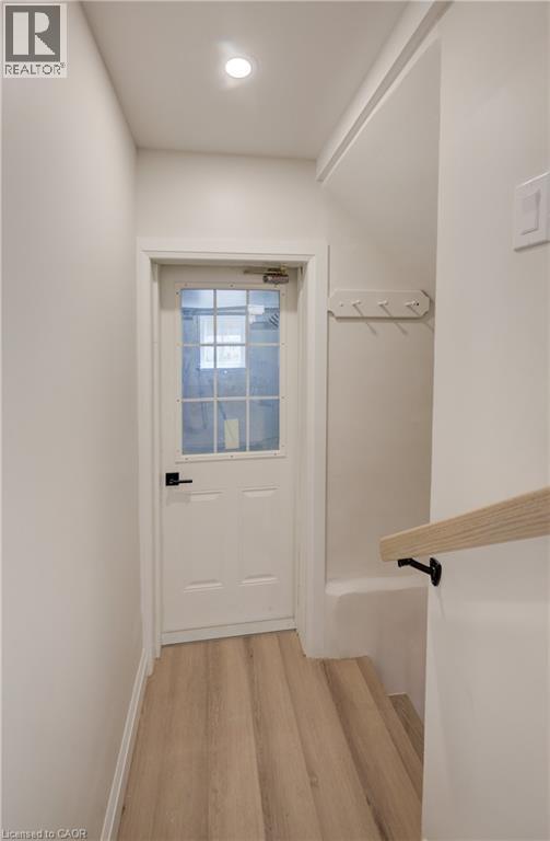 Recessed ceiling lighting, wood-finish flooring, white paneled door with window, black door hardware, and wood handrail with black brackets - 34 Moore Avenue N, Waterloo, ON - Indoor Photo Showing Other Room