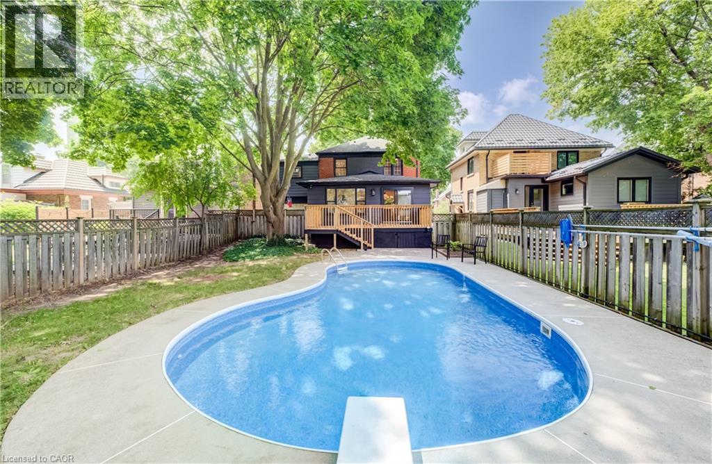 Curved inground pool with a diving board, surrounding concrete patio, and a tiered wood deck - 34 Moore Avenue N, Waterloo, ON - Outdoor With In Ground Pool With Deck Patio Veranda With Backyard
