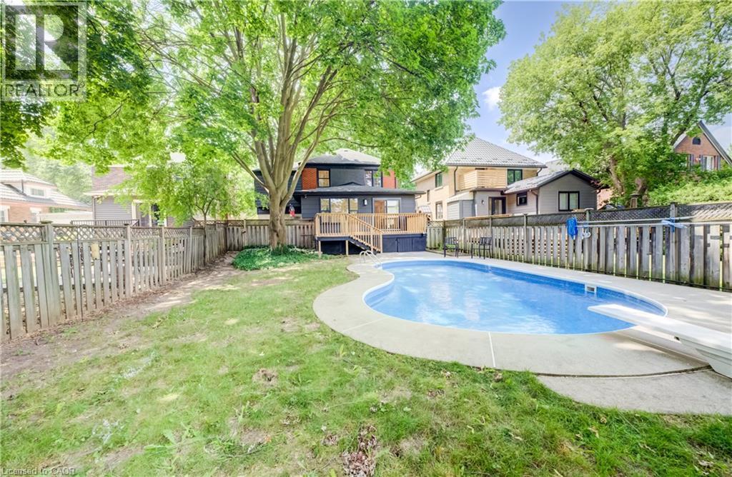 Rear exterior featuring a freeform swimming pool with concrete coping, a wooden deck, and a privacy fence - 34 Moore Avenue N, Waterloo, ON - Outdoor With In Ground Pool With Backyard