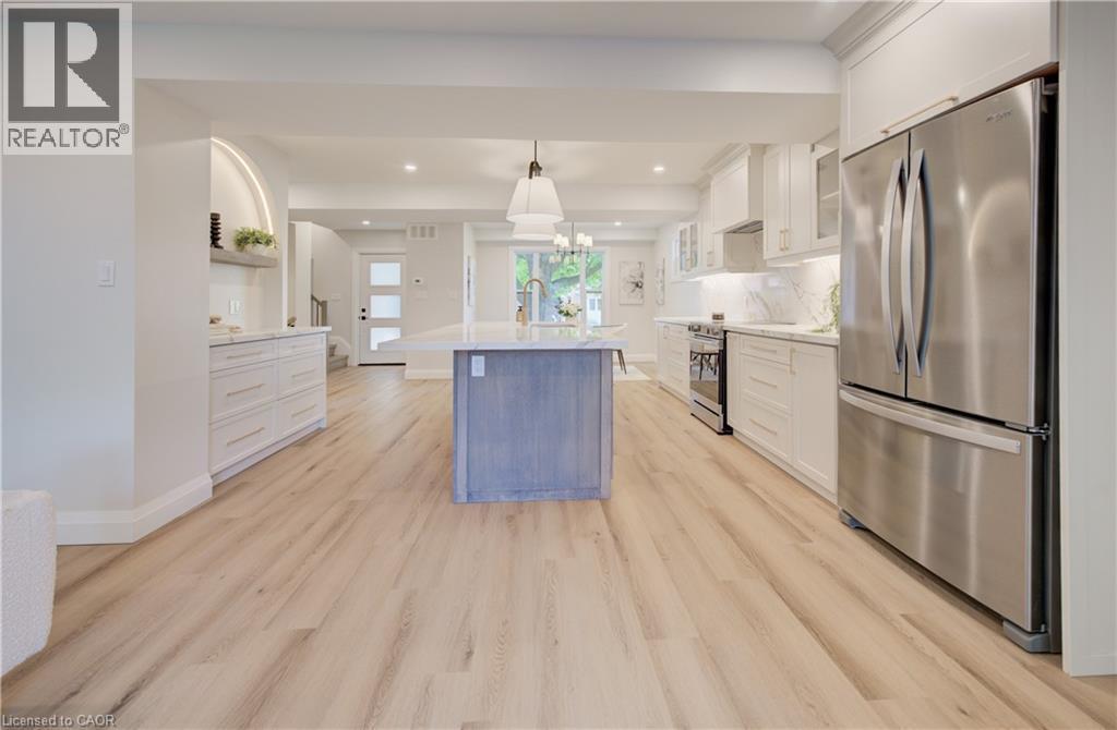 Open-concept kitchen featuring wood-finish flooring, a central island with a sink, white cabinetry, stainless steel appliances, and recessed lighting - 34 Moore Avenue N, Waterloo, ON - Indoor Photo Showing Kitchen With Stainless Steel Kitchen