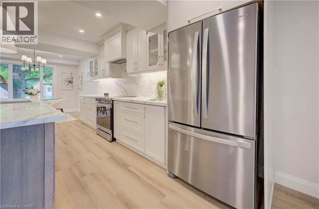 Stainless steel French door refrigerator, white cabinetry with gold-tone hardware, wood-finish flooring, white marble-look countertops, and recessed lighting - 34 Moore Avenue N, Waterloo, ON - Indoor Photo Showing Kitchen With Stainless Steel Kitchen With Upgraded Kitchen