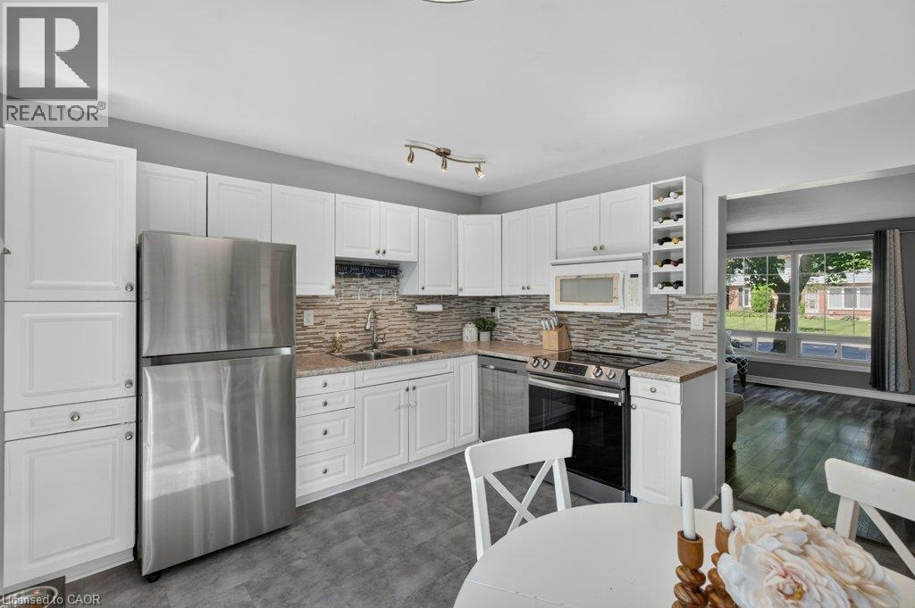 Kitchen featuring white cabinetry, stainless steel appliances, a textured tile backsplash, and light-toned countertops - 60 Elford Crescent, Hamilton, ON - Indoor Photo Showing Kitchen With Double Sink With Upgraded Kitchen