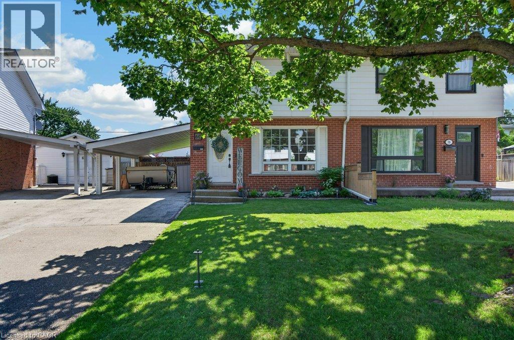 Charming brick ranch home featuring a mature shade tree canopy, manicured lawn, covered front entry with transom window detailing, and attached carport with concrete driveway - 60 Elford Crescent, Hamilton, ON - Outdoor
