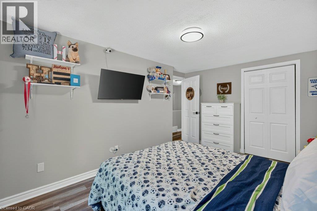 Warm gray wall color, wood-finish flooring, white bi-fold closet doors, white paneled interior door, and a flush-mount ceiling light - 60 Elford Crescent, Hamilton, ON - Indoor Photo Showing Bedroom