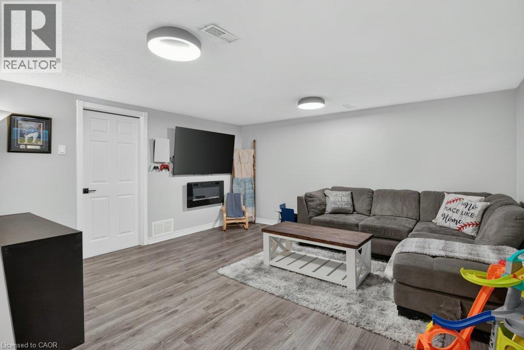 Wood-finish flooring, white paneled door with black hardware, wall-mounted television, and a built-in electric fireplace - 60 Elford Crescent, Hamilton, ON - Indoor Photo Showing Living Room With Fireplace
