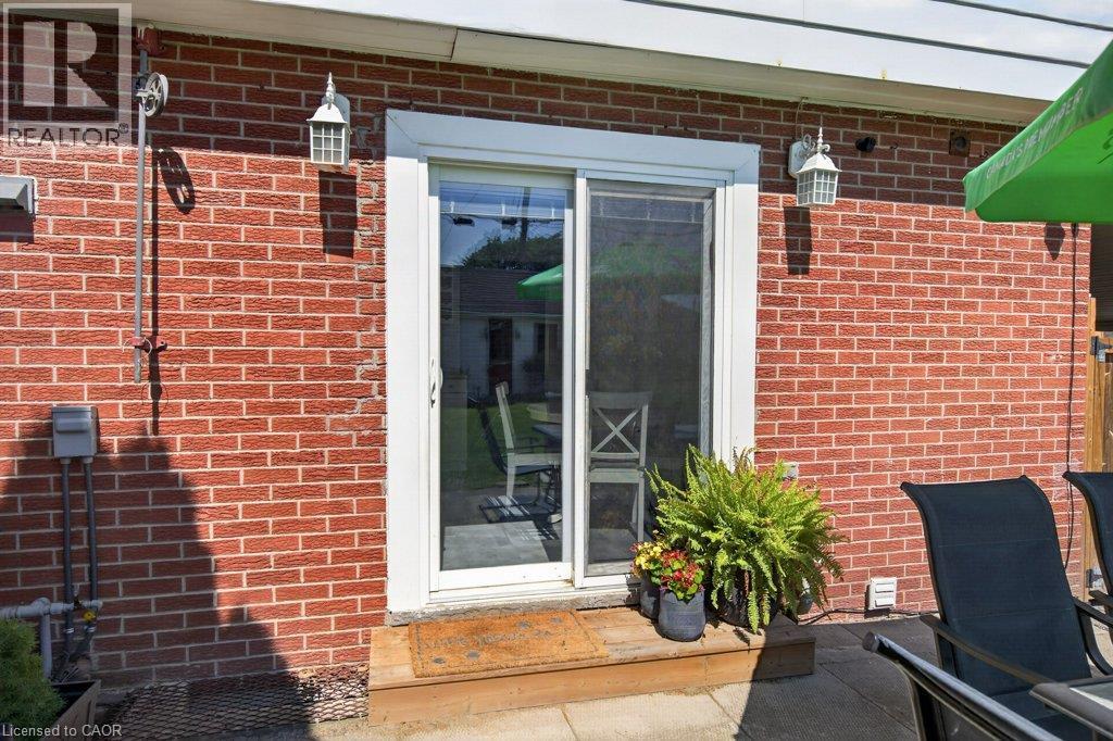 Brick exterior with a white-framed sliding glass door, dual exterior wall sconces, and a patio area - 60 Elford Crescent, Hamilton, ON - Outdoor With Exterior