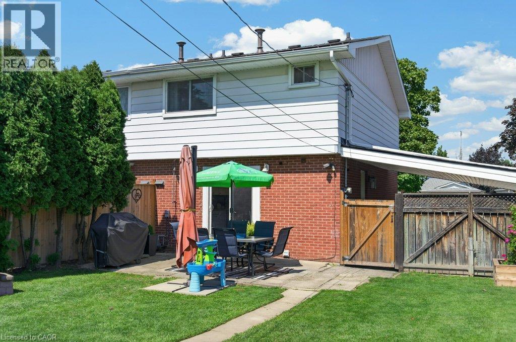 Expansive backyard with a manicured lawn, concrete patio, privacy fencing, and mature trees - 60 Elford Crescent, Hamilton, ON - Outdoor With Exterior