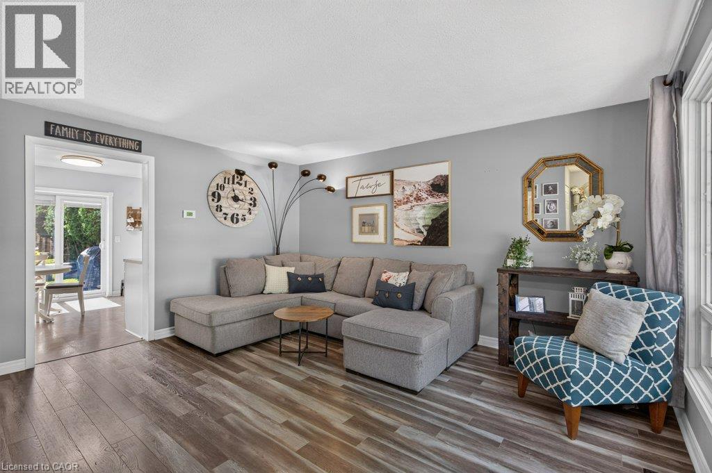 Bright living room showcasing hardwood flooring, a gray upholstered sectional sofa, and abundant natural light from multiple windows - 60 Elford Crescent, Hamilton, ON - Indoor Photo Showing Living Room