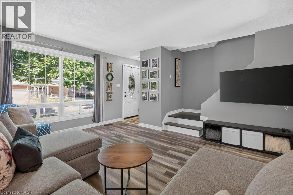 Spacious living area featuring wood-finish flooring, a large multi-pane window, and a white front entry door with an oval glass insert - 60 Elford Crescent, Hamilton, ON - Indoor Photo Showing Living Room