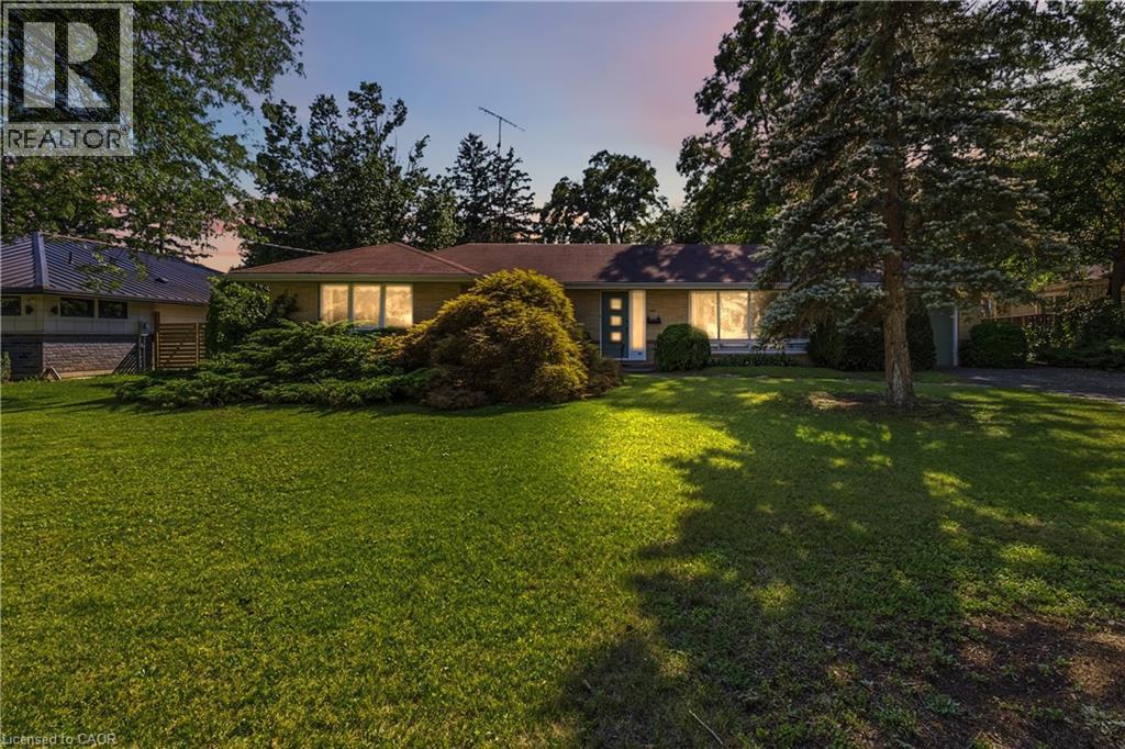 Single-story residence featuring a classic facade, a prominent front lawn, mature trees, and established foundational plantings - 974 Unsworth Avenue, Burlington, ON