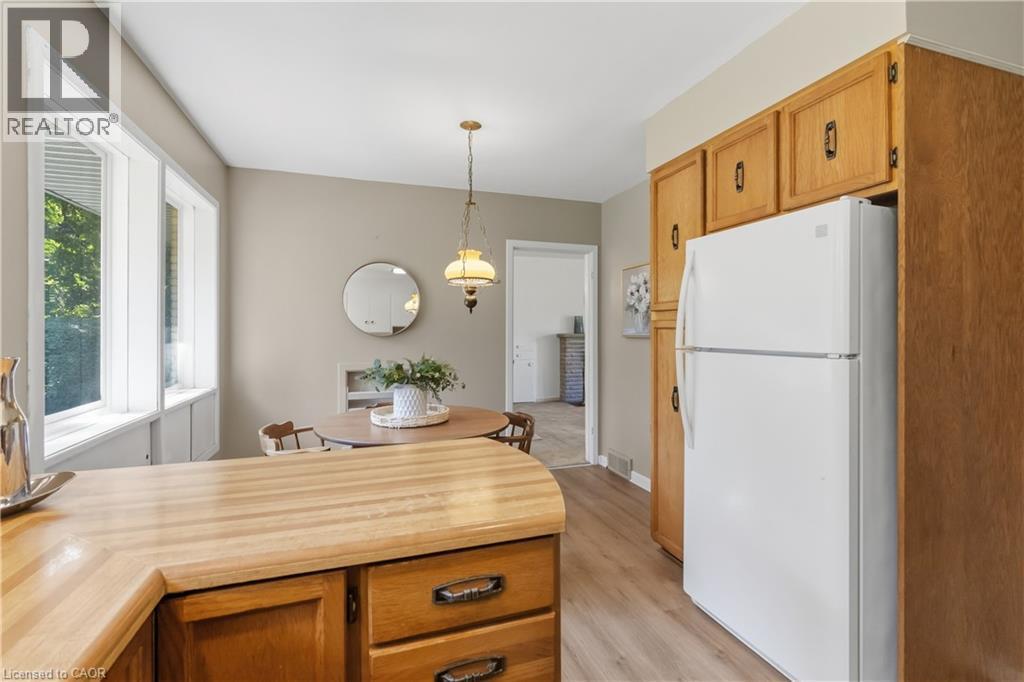 Bright and spacious kitchen featuring natural wood cabinetry with ample storage, a wood-finish island with drawers, stainless steel appliances including a refrigerator, and pendant lighting - 974 Unsworth Avenue, Burlington, ON