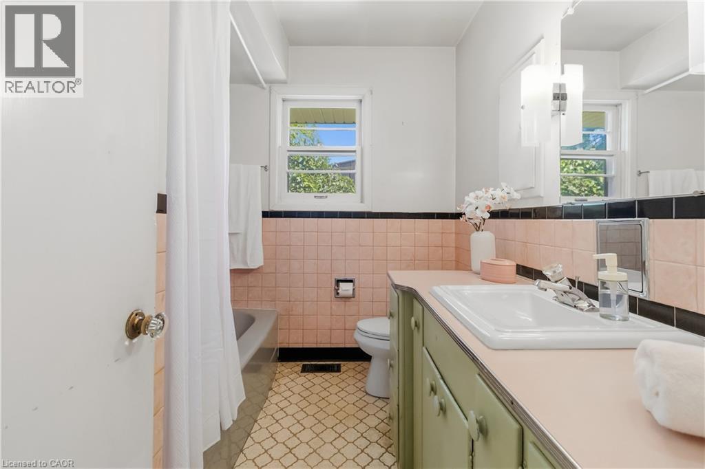 Charming bathroom featuring vintage pink tile walls, black and white tile accents, and a wood-finish vanity with integrated sink - 974 Unsworth Avenue, Burlington, ON