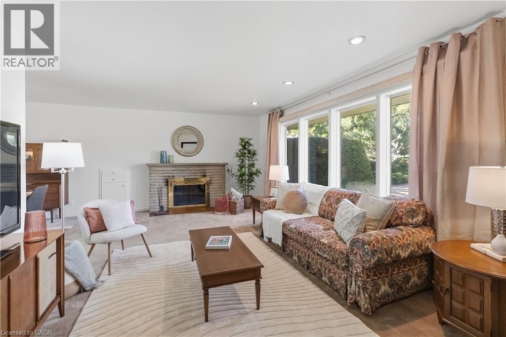 Spacious living area featuring a brick fireplace with a brass firebox, expansive windows, recessed ceiling lights, and light-toned carpet flooring - 974 Unsworth Avenue, Burlington, ON