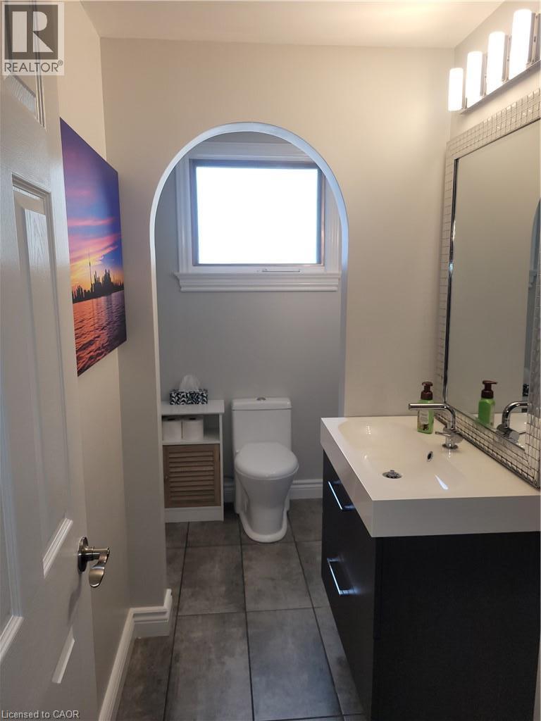 Modern bathroom featuring a sleek white rectangular vessel sink with matte black wall-mounted faucet, floating vanity with integrated storage, and contemporary toilet - 23 Bentley Place, Hamilton, ON - Indoor Photo Showing Bathroom