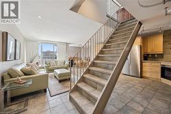 Multi-level interior featuring a tile staircase with metal railings, recessed lighting, and a kitchen area with wood cabinetry and stainless steel appliances - 