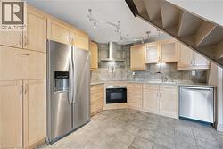 Modern kitchen featuring light wood cabinetry, stainless steel side-by-side refrigerator with ice/water dispenser, and matching stainless steel appliances including a built-in wall oven and dishwasher - 