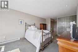 Spacious bedroom featuring a wrought iron bed frame, carpeted flooring, recessed ceiling lighting, and a large glass block window - 