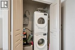 Dedicated laundry closet featuring stacked front-load washers and dryers with chrome shelving above, wall-mounted ironing board, and ample storage for cleaning supplies and linens - 