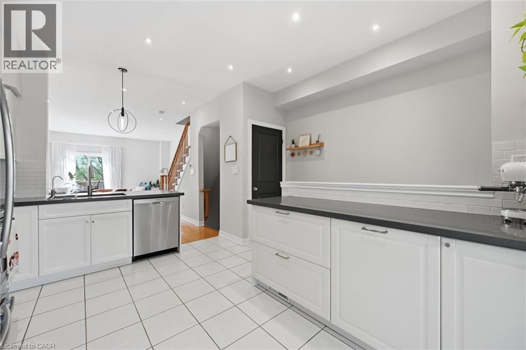 Modern kitchen featuring white cabinetry, dark countertops, a stainless steel dishwasher, and tile flooring - 678 Rowley Common, Burlington, ON - Indoor Photo Showing Kitchen