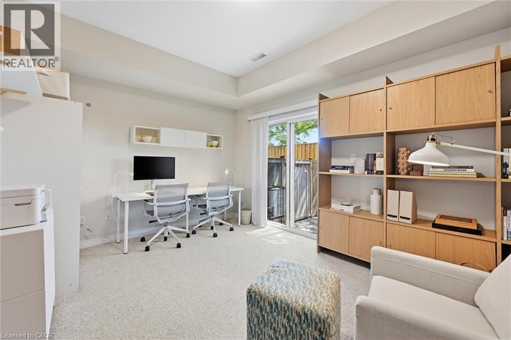 Light-toned room featuring a built-in wood-finish shelving unit, neutral carpet flooring, and a sliding glass door providing exterior access - 678 Rowley Common, Burlington, ON - Indoor Photo Showing Other Room