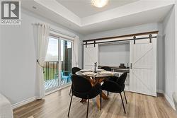 Dining area with a barn door, light wood-type flooring, and a raised ceiling - 