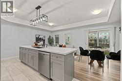 Kitchen with a tray ceiling, gray cabinetry, stainless steel dishwasher, hanging light fixtures, and open floor plan - 