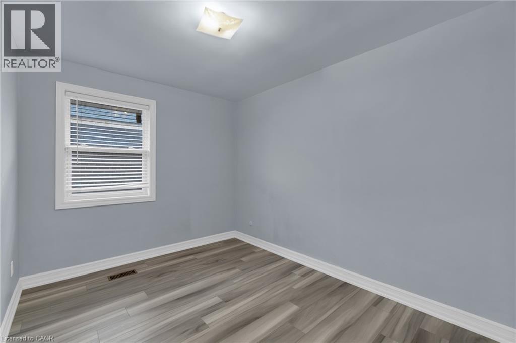 Room featuring light gray walls, wood-finish flooring, white baseboards, and a white-framed window with horizontal blinds - 197 Troy Street, Mississauga, ON - Indoor Photo Showing Other Room