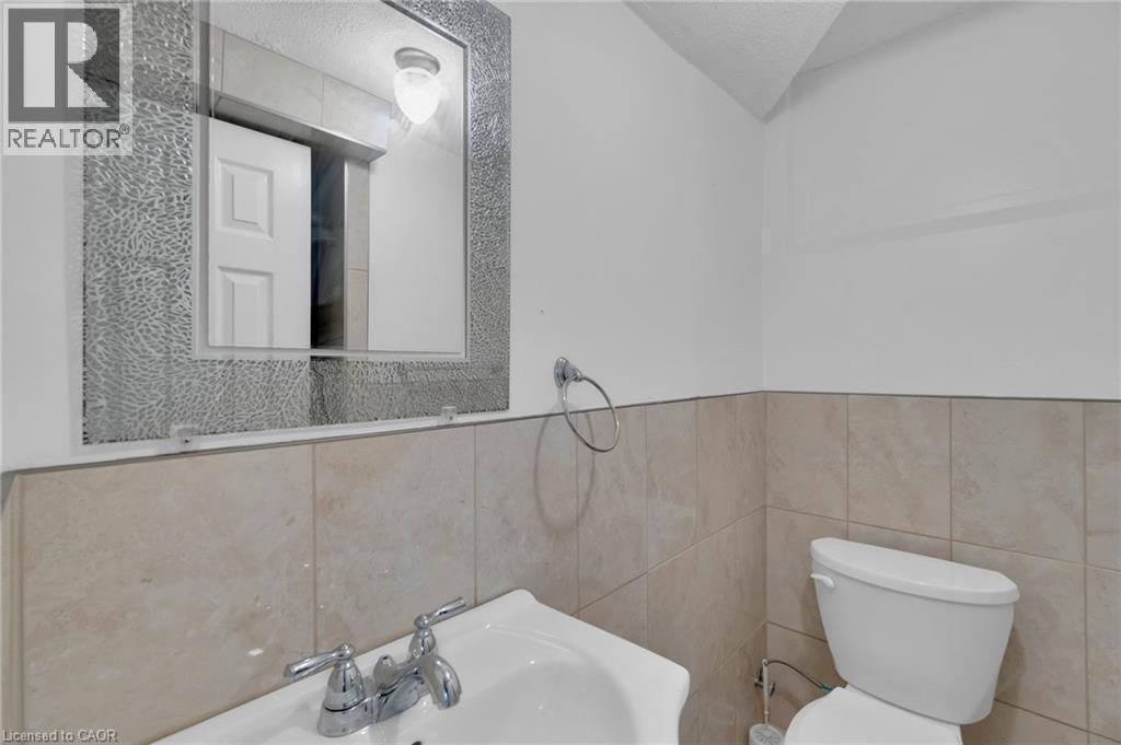 Bathroom featuring a decorative-framed mirror, wall-mounted light fixture, pedestal sink with chrome faucet, and tiled wainscoting - 197 Troy Street, Mississauga, ON - Indoor Photo Showing Bathroom