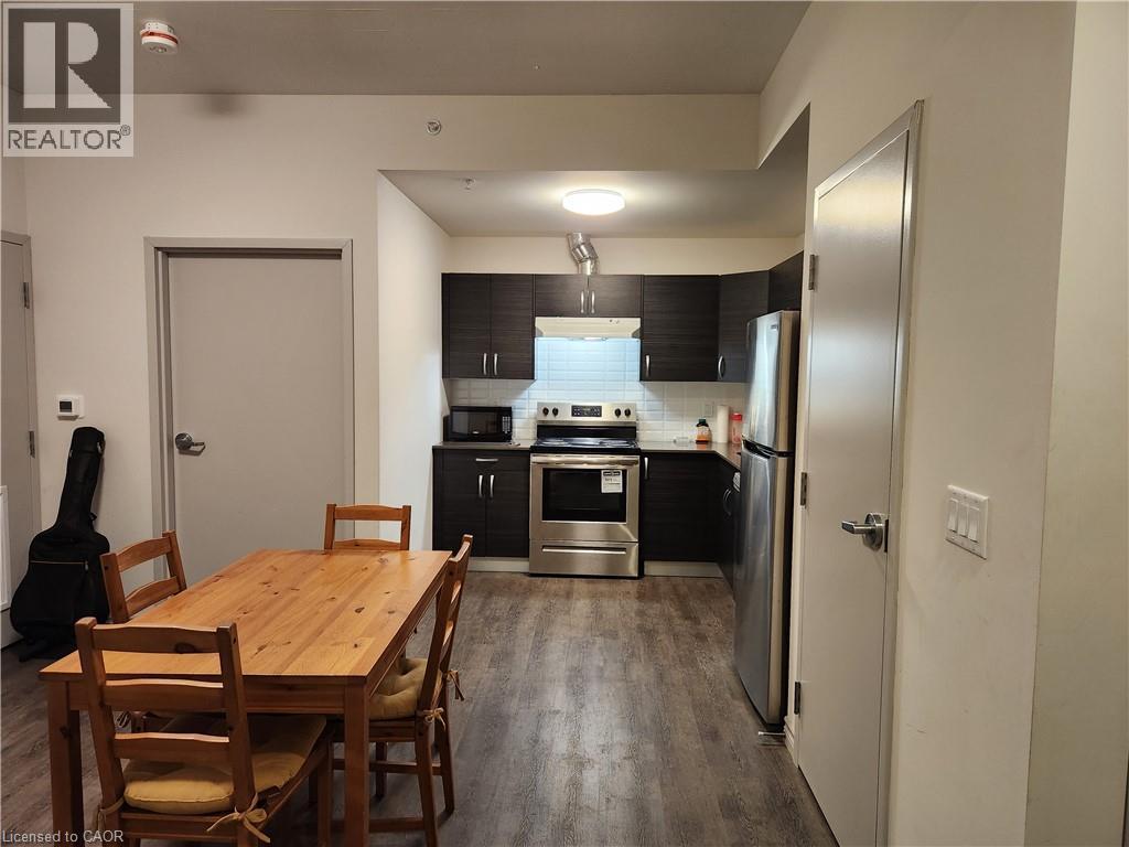 Kitchen with under cabinet range hood, dark wood-type flooring, appliances with stainless steel finishes, dark cabinetry, and decorative backsplash - 269 Sunview Street Unit# 607, Waterloo, ON - Indoor