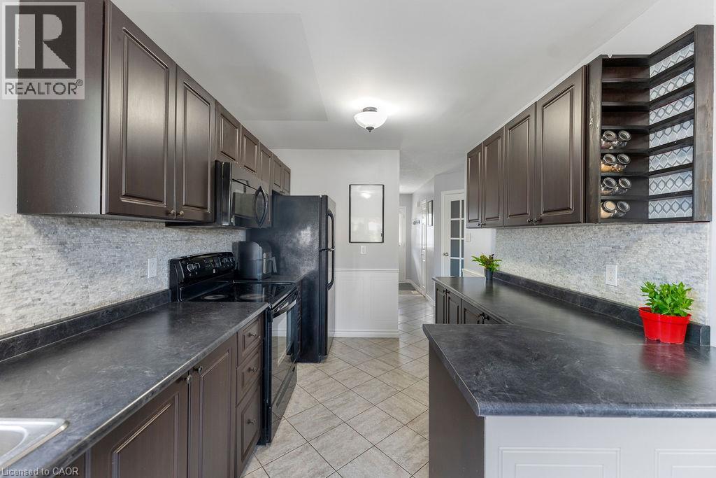 Galley kitchen featuring dark wood-finish cabinetry, black countertops, and a full tile backsplash - 33 Remple Court, Cambridge, ON - Indoor Photo Showing Kitchen