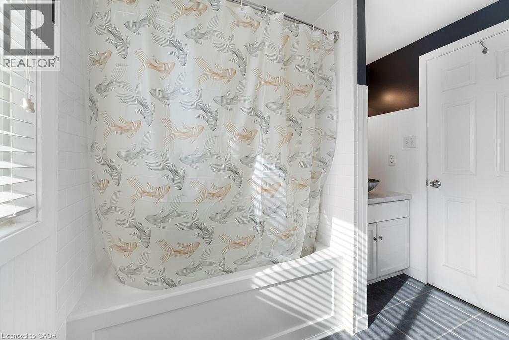 Bathroom featuring a white bathtub with subway tile surround, white paneled walls, and a window with horizontal blinds - 33 Remple Court, Cambridge, ON - Indoor Photo Showing Bathroom